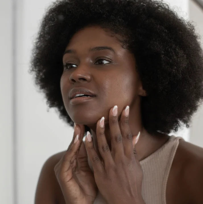 Woman with an afro touching her face against a neutral background | Makari de Suisse Uganda