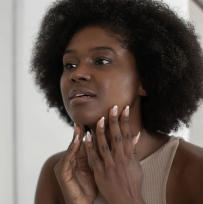 Woman with an afro touching her face against a neutral background | Makari de Suisse Uganda